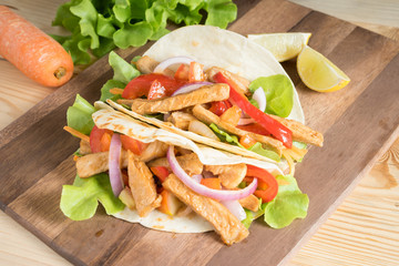 Obraz premium Grilled meat with onion and bell peppers, tomato,lettuce and serve with flour tortilla on wooden board.