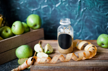 Vitamins, greens, vegetarianism, healthy food, sports. Apples, kiwi and smoothies from them on a dark background. Apple smoothies on a wooden tray with a centimeter. Bottle with black inscription for 