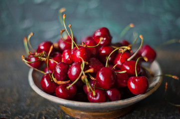 Ripe juicy cherry and cherry on a dark gilded background in a plate. Vitamins, greens, vegetarianism, healthy food, sports.