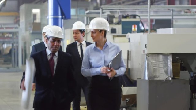 Group of architects visiting factory. Woman in hardhat talking with colleague and senior businessman telling about industrial process