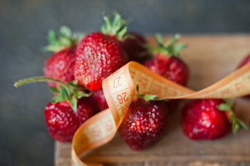 Ripe juicy strawberries on a dark gilded background in a dish with a centimeter. Vitamins, greens, vegetarianism, healthy food, sports.