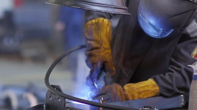 Tilt down shot of industrial worker in protective mask and gloves welding metal with gas torch in slow motion