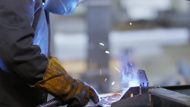 Tilt up of welder in protective wear using gas torch for welding metal material in slow motion