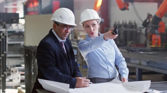 Tracking shot of male and female executive engineers working together on architectural plan in factory workshop. Slow motion footage