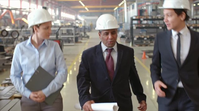 Latin American executive engineer in hardhat walking in factory and talking with male and female colleagues