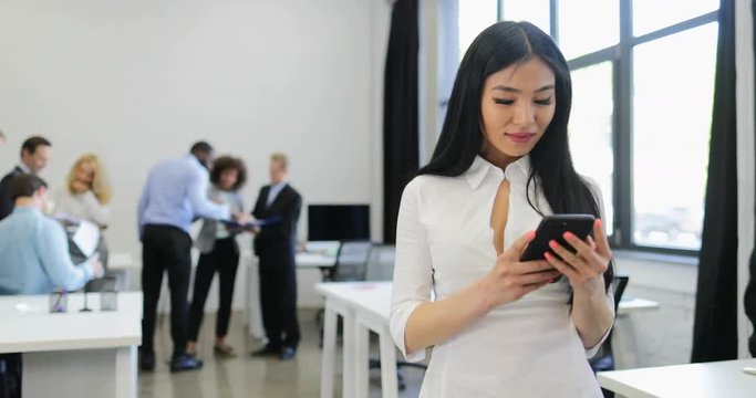 Asian Businesswoman Hold Smartphone Chatting Online In Modern Office During Meeting Of Business People Group Coworking On Background Slow Motion 60