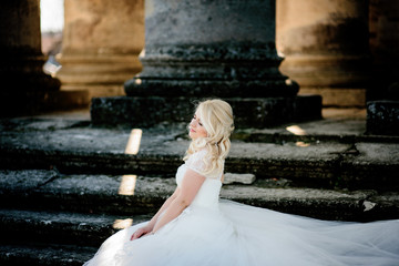 Bride sits on ruined footsteps in rays of evening light