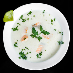 Fish soup with salmon and shrimps, parsley and lemon in bowl, isolated on black background, healthy food. Top view