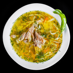 Chicken soup - broth with noodles, herbs and vegetables in bowl, isolated on black background, healthy food. Top view