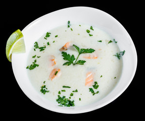 Fish soup with salmon and shrimps, parsley and lemon in bowl, isolated on black background, healthy food. Top view