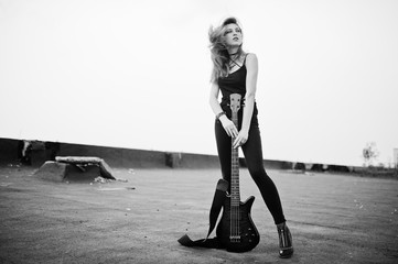 Red haired punk girl wear on black with bass guitar at the roof.