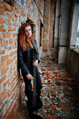 Red haired punk girl wear on black with bass guitar at abadoned place. Portrait of gothic woman...