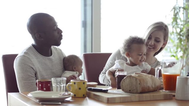 Young interracial family with little children having breakfast.