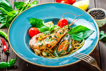 Italian pasta spaghetti with seafood, langoustine, mussels, squid, scallops, shrimp, Parmesan cheese, fresh basil and tomatoes on rustic wooden background. Mediterranean food. Top view