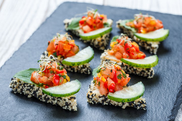 Appetizer canape with chopped vegetables and sesame on stone slate background close up. Delicious snacks, sandwiches, crostini, bruschetta, antipasti on party or picnic time. Top view