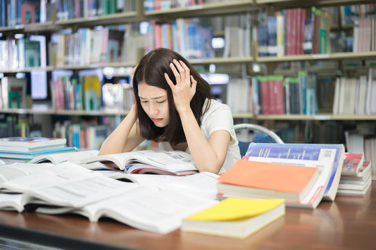 Young Asian student under mental pressure while reading book preparing examination in library at university. Asian student looking stressed..