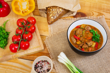 Stew with meat and vegetables in tomato sauce on wooden background