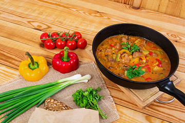 Stew with meat and vegetables in tomato sauce on wooden background