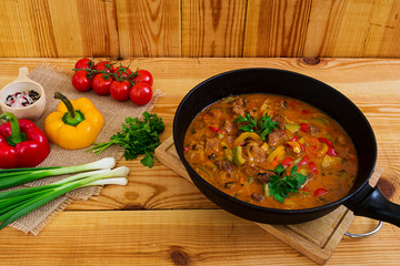 Stew with meat and vegetables in tomato sauce on wooden background