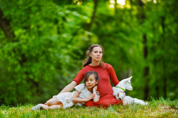 The girl and her little goat rest lying at the knees of the mother. They sit on the grass of a small hill in the middle of the forest