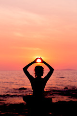 Woman silhouette sitting in lotus position on sunset sea background back lit