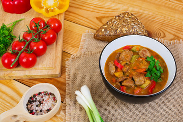 Stew with meat and vegetables in tomato sauce on wooden background