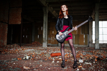 Red haired punk girl wear on black and red skirt, with bass guitar at abadoned place. Portrait of...