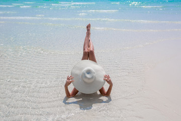 Obraz premium Woman in white hat lying on the beach, blue sea and sky background