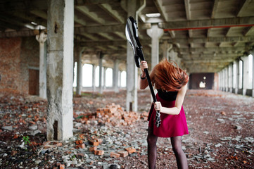 Red haired punk girl wear on black and red skirt, with bass guitar at abadoned place. Portrait of...