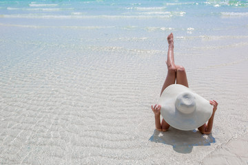 Fototapeta na wymiar Woman in white hat lying on the beach, blue sea and sky background