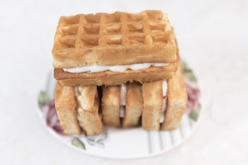 Three Viennese waffles with a cream filling and one wafer on top lie on a white saucer with a floral pattern on a white background