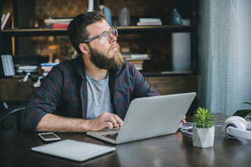 pensive bearded man typing on laptop while sitting at home