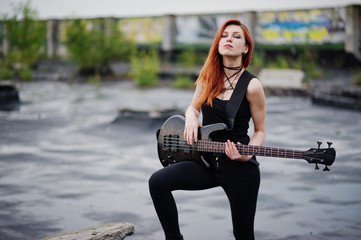 Red haired punk girl wear on black with bass guitar at the roof.