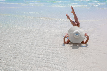 Woman in white hat lying on the seashore in water, blue sea and sky background
