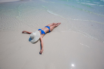 Woman in white hat lying on the seashore in water, blue sea and sky background