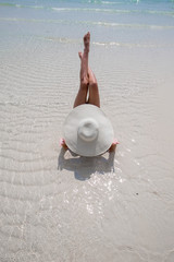 Fototapeta na wymiar Woman in white hat lying on the seashore in water, blue sea and sky background