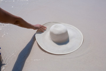 Female hand holding white hat on the beach