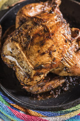 Grilled chicken lies in a black frying pan on a multi-colored striped background, vertical frame.