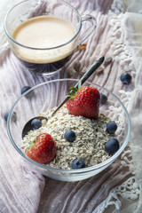 Usual breakfast: glass bowl with flakes and berries, cup of black coffee on the pink tissue