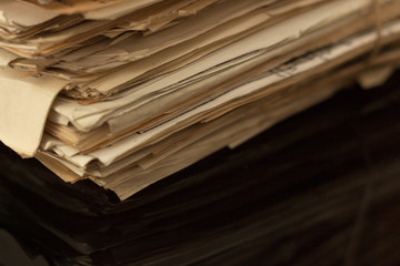 Old dusty stack of papers, documents on black reflective ground