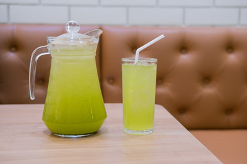 Glass of iced green tea and jug of iced green tea on wood table