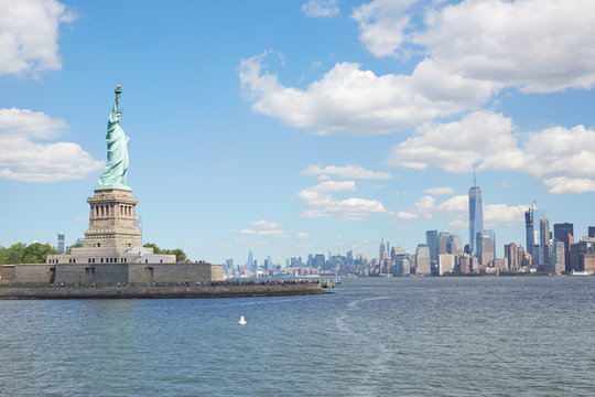 Statue of Liberty island and New York city skyline in a sunny day, white clouds
