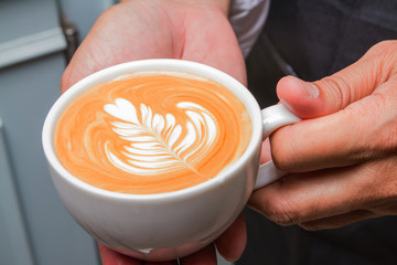 Barista holding cup latte art coffee in cafe.