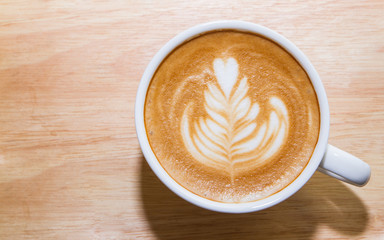 A cup of coffee with heart pattern in a white cup on wooden background