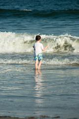 Young cute little boy playing at the seaside running into the surf on a sandy beach in summer sunshine