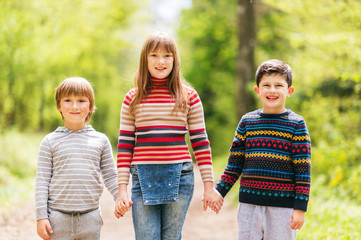 Group of three happy kid hiking in spring forest, two boys and one girl playing together outside, wearing pullovers