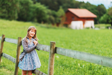 Naklejka premium Pretty kid girl playing in a beautiful summer park at sunset, resting on a fence, happy childhood in countryside