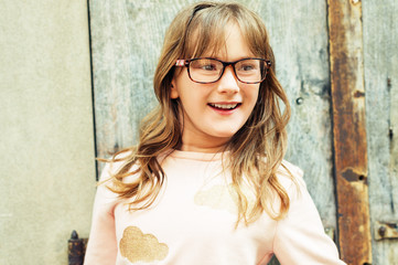 Fototapeta premium Outdoor portrait of a cute little 9 year old girl, wearing soft pink sweatshirt and glasses