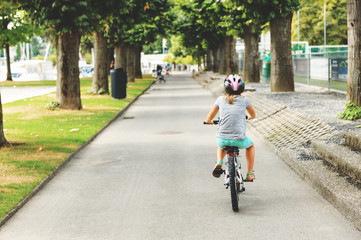 Kid girl riding bicycle in the park, back view