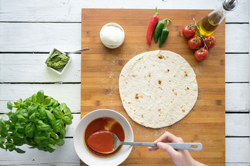 Traditional Italian pizza dough flat bread making tomato sauce mozzarella cheese salami prosciutto ham sausage basil hands chef wooden board kitchen preparation